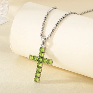 Macro detail of cross pendant with green stones on a polished silver chain