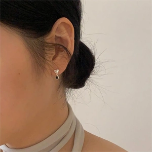 Close-up of minimalist silver heart studs with black round pendants worn by a model