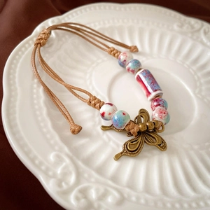 Vintage woven bracelet with ceramic beads and a bronze butterfly charm on a white plate