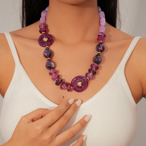 Detail view of purple acrylic beaded necklace with gold spacers on white ribbed top