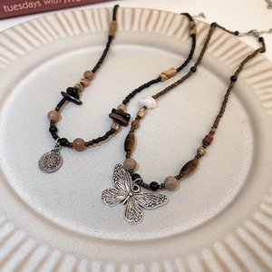 Detailed shot of beaded necklaces with butterfly and sun-moon pendants on ceramic tray