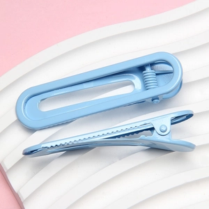 Detail of two light blue metal duckbill hair clips on a white textured stone surface