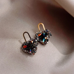 Macro shot of heart-shaped earrings with dark crystals and golden hooks on silk fabric
