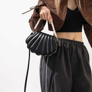 Detail of black shell crossbody bag with large pearl handle and textured stripes