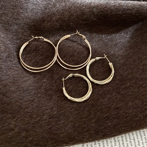 Close-up of gold hoop earrings with matte and twisted textures on brown fur background