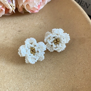 Detailed macro view of white beaded camellia flower earrings with golden pearl center pieces