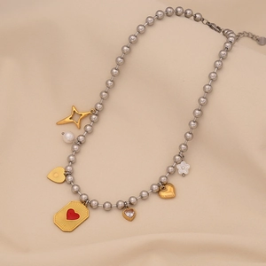 Detail of silver bead necklace with gold heart, star charms and white pearls on fabric
