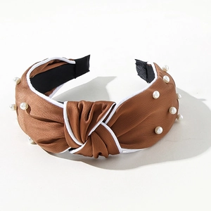 Close-up of brown satin knotted headband featuring decorative faux pearls and white piping