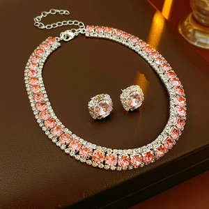 Detailed close-up of shiny pink crystal necklace and stud earrings set on leather
