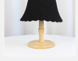 Detailed view of black knitted bucket hat with wavy brim on wooden stand
