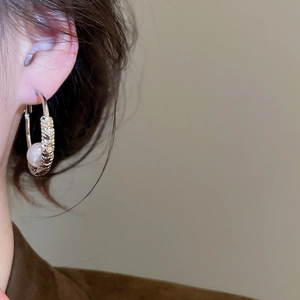 Close-up of model wearing silver spiral hoop earrings with round white pearl charm
