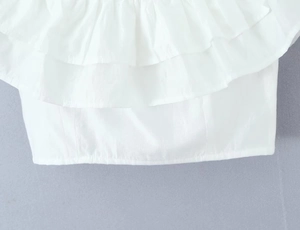 Detail of white ruffled off-shoulder top and embroidered skirt with woven fabric texture