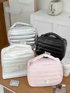 Quilted waterproof makeup bags in silver, black, white and pink on a wooden desk