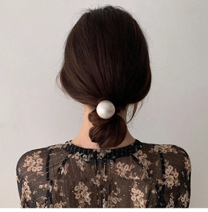 Dettaglio di un elastico per capelli con perla grande che fissa una coda di cavallo bassa