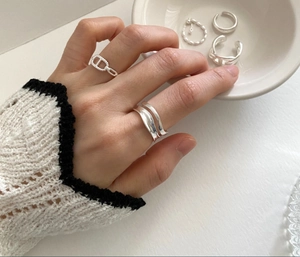 Detailed view of stacked 925 sterling silver minimalist wavy rings on a warm white surface