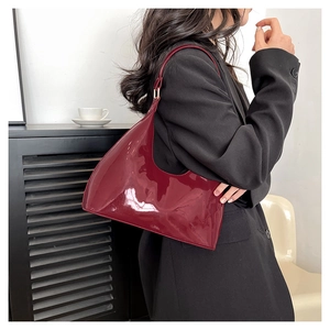 Detail of dark red glossy patent leather shoulder bag worn with a black blazer