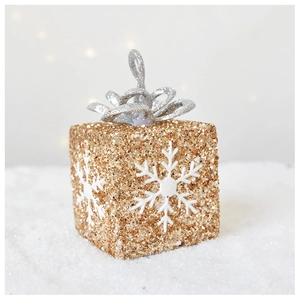 Close-up of golden Christmas gift box ornament with silver bow and white snowflakes