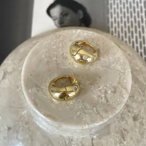 Macro shot of gold huggie earrings with star zircon inlays on a white marble display tray