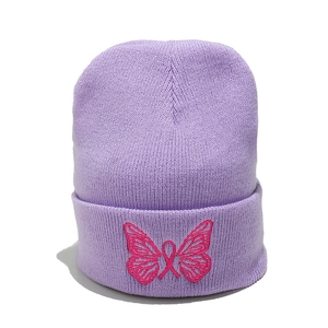 Dettaglio del berretto in maglia lavanda con ricamo di farfalla rosa e nastro