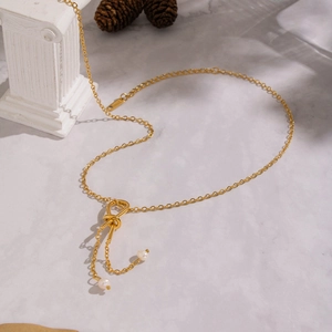 Detailed view of a gold knot necklace with freshwater pearls on a marble surface