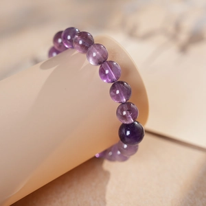 Makroaufnahme eines Amethyst-Perlenarmbands in Dunkelviolett auf einem Zylinder-Display