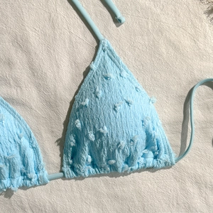 Dettaglio del top bikini azzurro con texture increspata e accenti floreali in 3D
