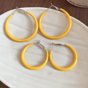 Détail de boucles d'oreilles créoles jaunes de deux tailles sur un plateau céramique