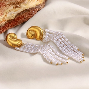 Détail de boucles d'oreilles à pompons dorés 18K avec perles blanches sur un socle en pierre