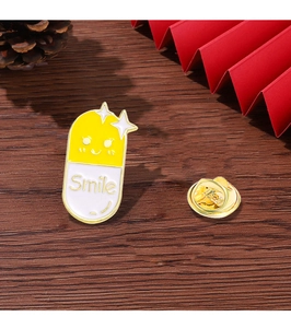 Detail of yellow and white capsule enamel pin with Smile text on wooden background