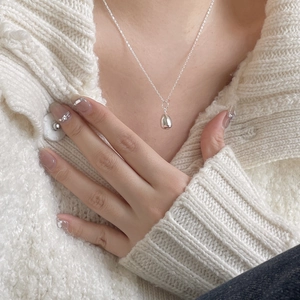 Close-up of a minimalist silver teardrop pendant necklace worn over a white knit sweater
