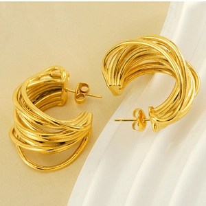 Detail view of gold multi-layered wire wrap C-shaped hoop earrings on elegant beige fabric