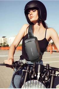 Detail of grey hardshell sling bag worn by a motorcyclist in an outdoor urban setting