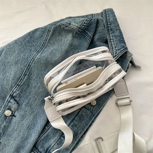 Modern white transparent PVC crossbody jelly bag with wide fabric strap on denim jacket