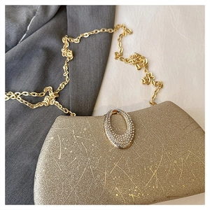 Detailed view of a gold evening bag featuring a rhinestone-encrusted oval buckle and chain
