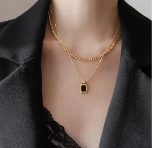 Close-up of double layered gold necklace featuring a black square pendant on model