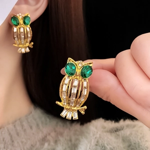 Detailed close-up of golden owl earrings with green gem eyes and rectangular diamonds