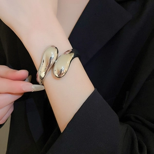 Dettaglio di un bracciale a polsino in metallo liquido argento con design organico al polso