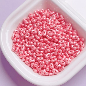 Macro view of pink peanut-shaped acrylic beads with pearlescent finish in a white bowl