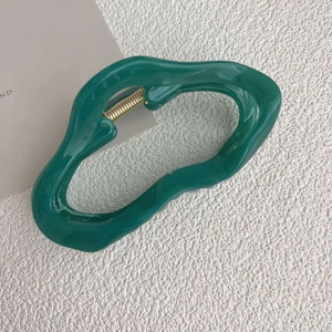 Detail of emerald green wavy hair claw clip with golden metal spring on a white surface