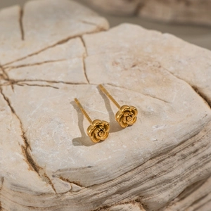 Macro shot of elegant golden rose studs resting on a natural textured stone surface