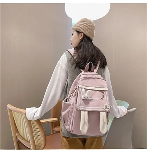 Pink backpack with 3D rabbit ears and fluffy charm shown in a cozy indoor setting