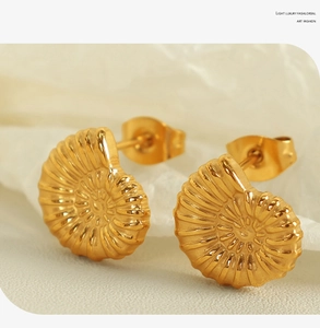 Macro detail of gold-plated seashell stud earrings with spiral textured pattern