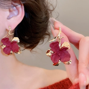 Detailed close-up of matte burgundy flower earrings with elegant gold branch accents