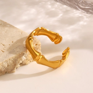 Golden stainless steel bamboo style open ring displayed on stone with water reflections