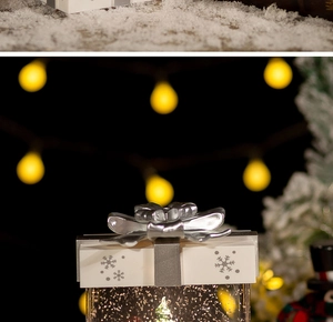 Close-up of silver Christmas gift box snow globe with a bow and warm bokeh background