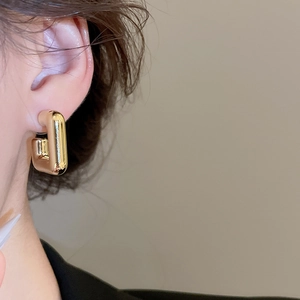Vue détaillée d'une boucle d'oreille rectangulaire dorée polie portée par un mannequin
