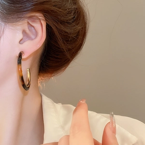 Close-up of tortoise shell resin hoop earrings with gold metal lining on female model