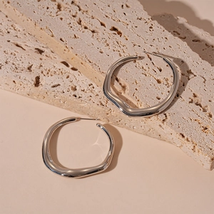 Macro detail of silver liquid metal irregular geometric hoop earrings on stone