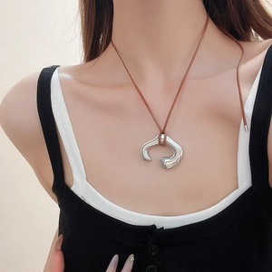 Close-up of irregular silver crescent pendant with brown leather cord on a model