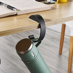 Portable black desk side bag hook for students, hanging a water bottle on a wooden table